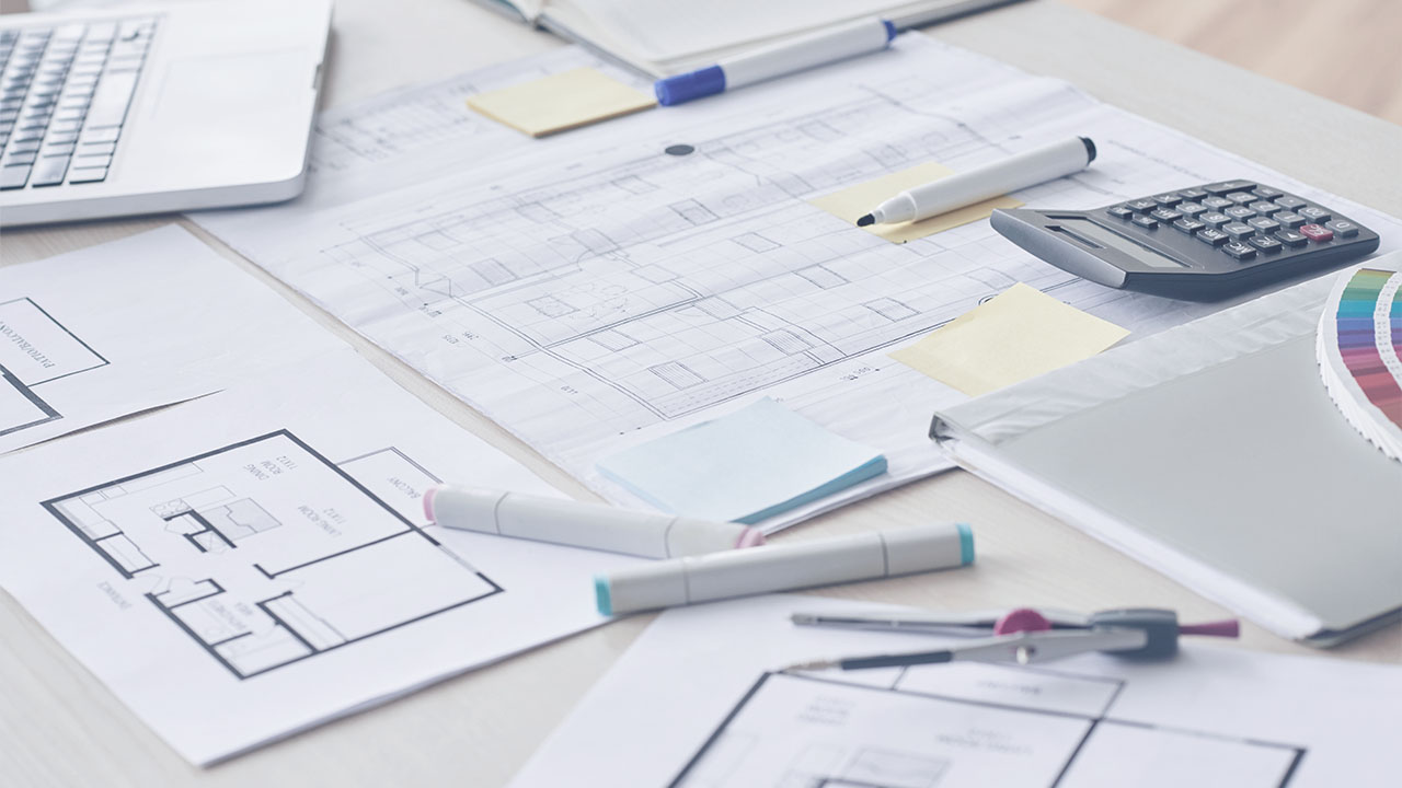 Imagen de un primer plano de un plano arquitectónico, con lápices y calculadoras sobre un escritorio