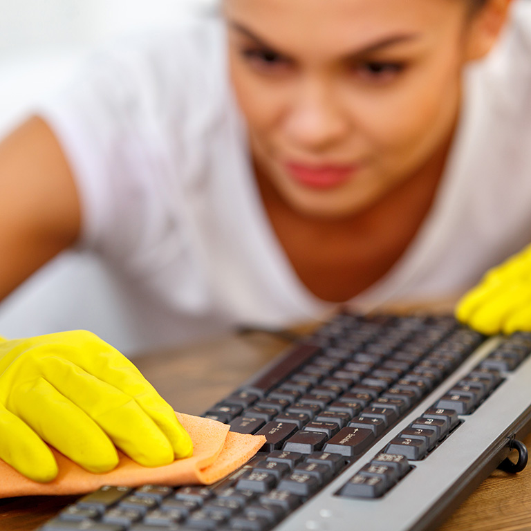 Imagen de una mujer con traje de limpieza y guantes amarillos limpiando un teclado con un paño