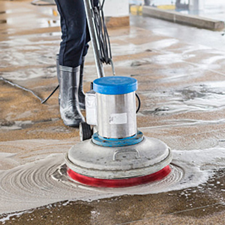 Imagen de una persona pasando una máquina abrillantadora de suelo con líquido y espuma limpiadora sobre el suelo