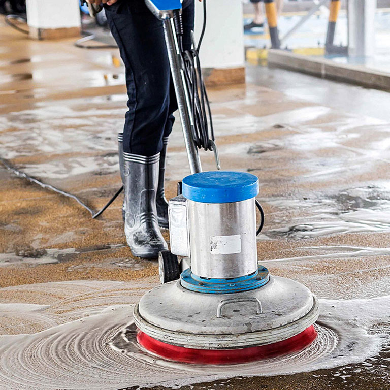 Imagen de una máquina limpiadora de pisos siendo operada por una persona con botas con jabón en el piso